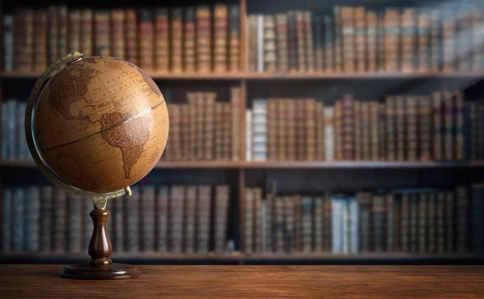 An antique globe on a wooden desk in front of a wall of old library books