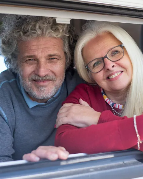 Grey Nomads & Snowbirds: a retired couple smiling from the window of their campervan on the road